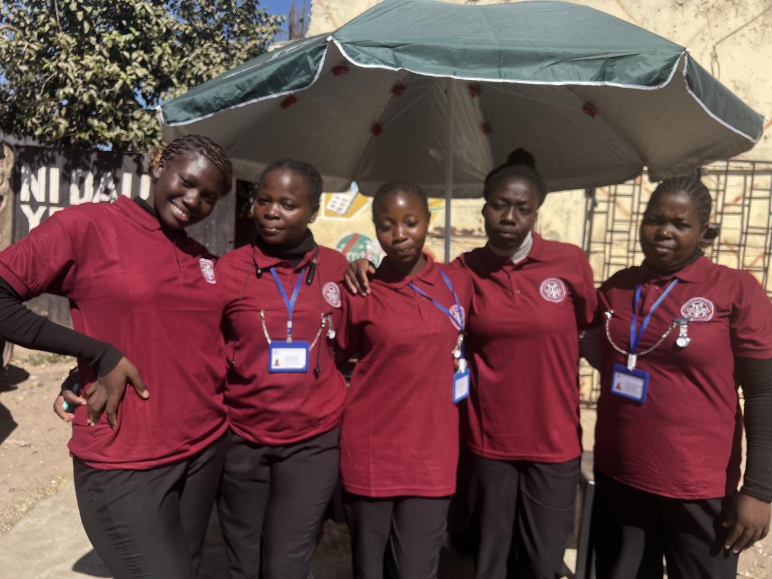 Five Fernwood caregivers in maroon uniforms with ID badges, trained in-house in Lusaka